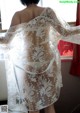 A woman wearing a white lace robe standing in front of a window.
