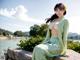 A woman in a green dress sitting on a stone wall.