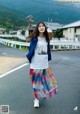 A woman in a white shirt and colorful skirt standing on a road.