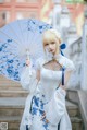 A woman in a white dress holding a blue and white umbrella.