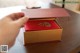 A person opening a red and gold box on a table.